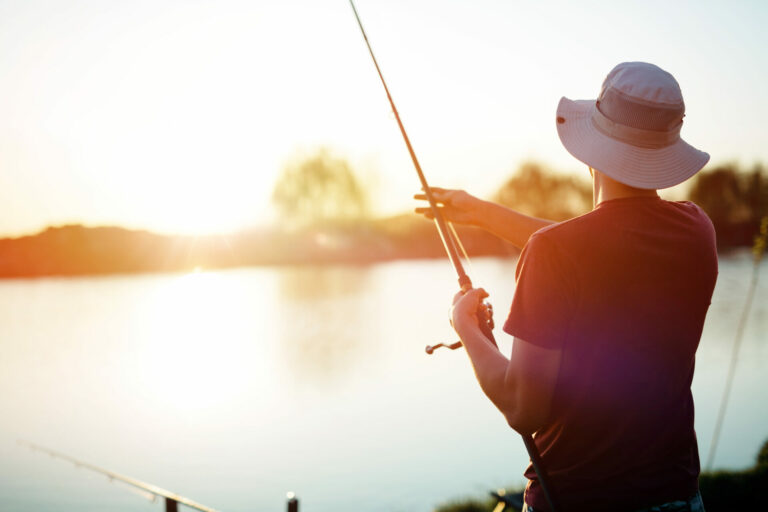 Junger Mann, der bei Sonnenuntergang an einem See fischt und Hobby genießt