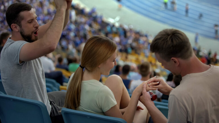 Man proposing marriage to girl at stadium, wearing engagement ri